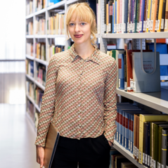 Eine Wissenschaftlerin steht in einer Bibliothek.