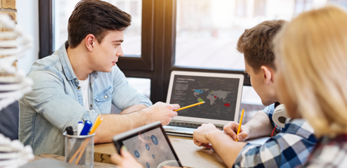 Drei Schüler:innen schauen auf einen Laptop, einer der Schüler zeigt auf eine digitale Karte.