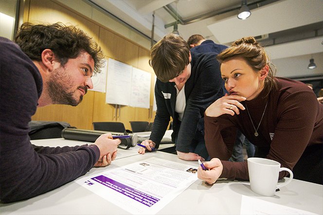 Foto: Malte Michelsen Drei Fellows sitzen an einem Tisch, auf dem ein Dokument liegt. Zwei der Fellows schauen sich nachdenklich an.