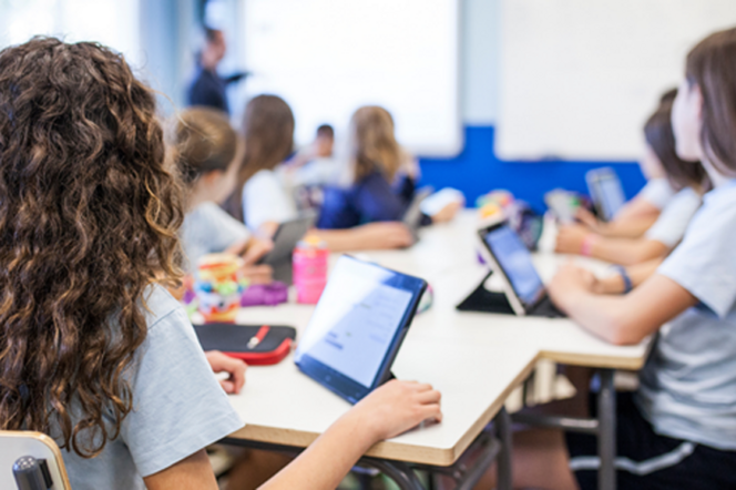 Schüler:innen einer Tabletklasse hören ihrem Lehrer zu.