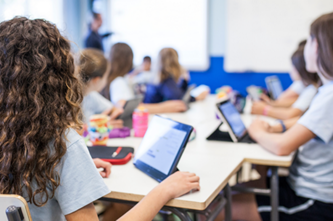 Schüler:innen einer Tabletklasse hören ihrem Lehrer zu. 