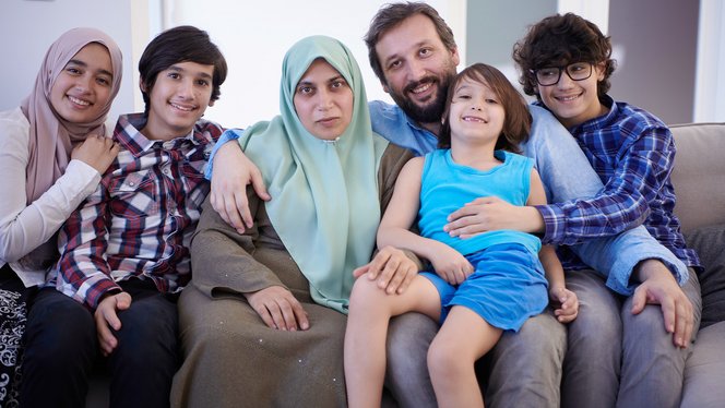 Eine Familie sitzt auf dem Sofa, ein Kind im Grundschulalter sitzt auf dem Schoß seines Vaters.