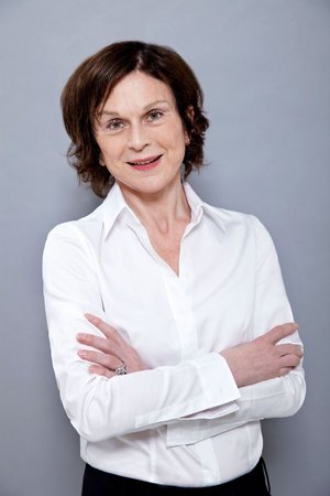 Inge Bliestle, ein Jury-Mitglied der "innovate! Akademie", schaut lächelnd in die Kamera. Sie hat verschränkte Arme, trägt eine weiße Bluse, der Hintergrund ist neutral grau.