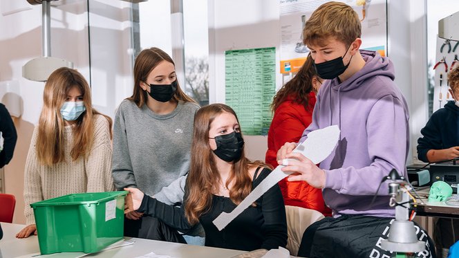 Drei Schülerinnen und ein Schüler schauen auf ein Bauteil für ihr Luft- und Raumfahrtprojekt.