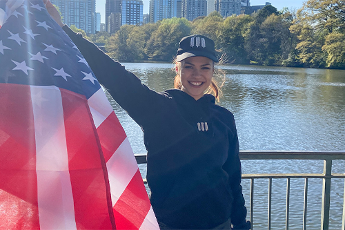 Die Auszubildende Anna Börner steht mit der US-amerikanischen Flagge vor einem See und einer Skyline.