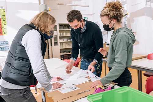 Drei Lehrkräfte schauen auf Baupläne für das Technikprojekt